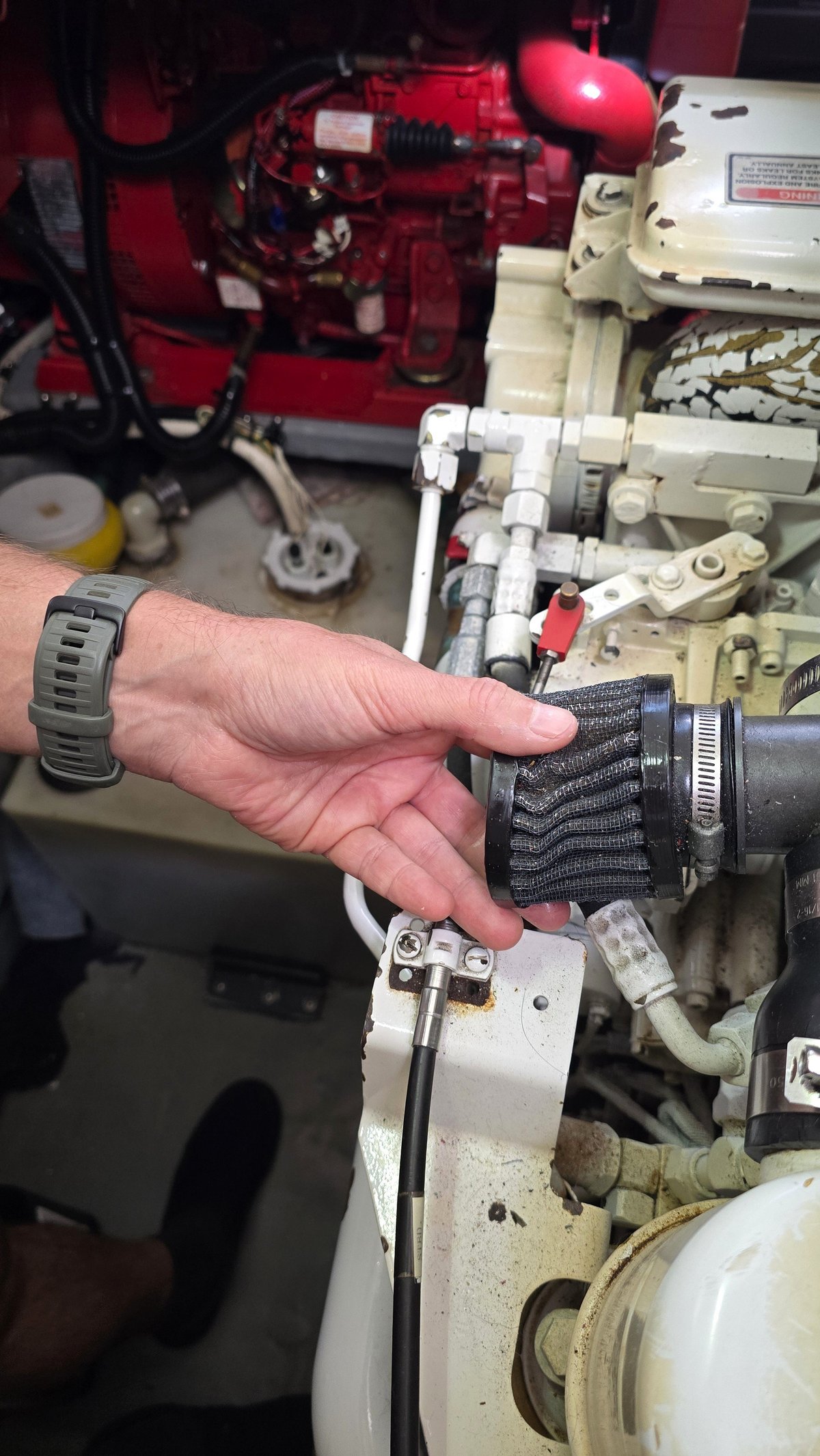 Mechanic's hand holding a small air filter during boat engine maintenance. Detailed view of marine engine components and mechanical parts.